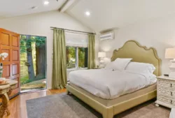 Plush king bed, bedside tables and lamps in a room with a peaked ceiling, with door open to treescottage-king-bed.jpg
